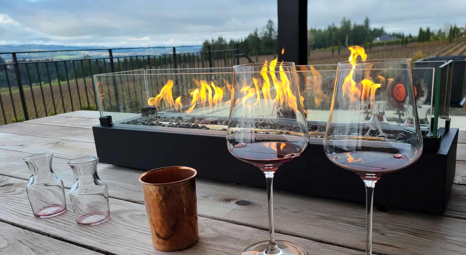 A cozy winter wine tasting at a Willamette Valley winery with wine glasses on a table outside with a tabletop fireplace.