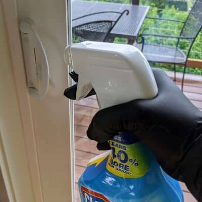 a gloved hand holding a bottle of clorox clean-up spraying a door handle