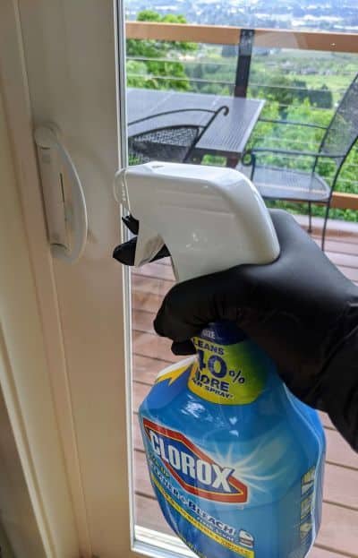 spray bottle of Clorox Clean-up held by a gloved hand, aimed at a door handle 