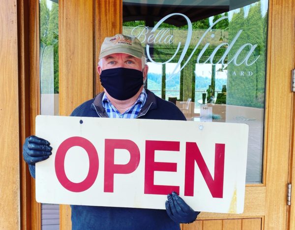 Steve Whiteside at Bella Vida tasting room holding a sign that says OPEN