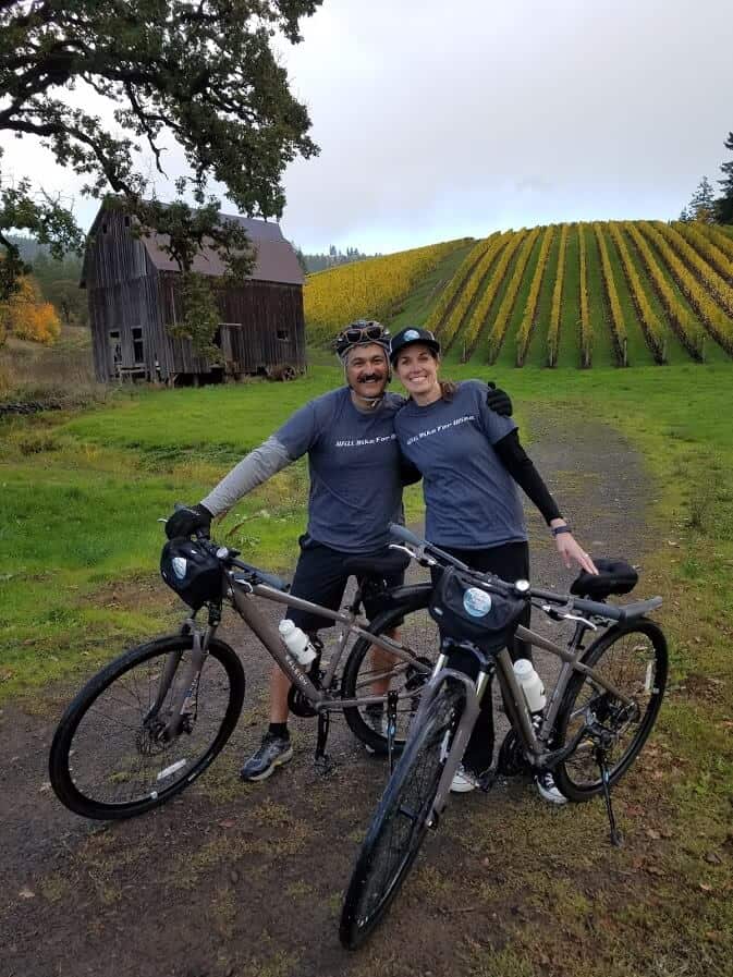 two people standing with bikes in front of a vineyard