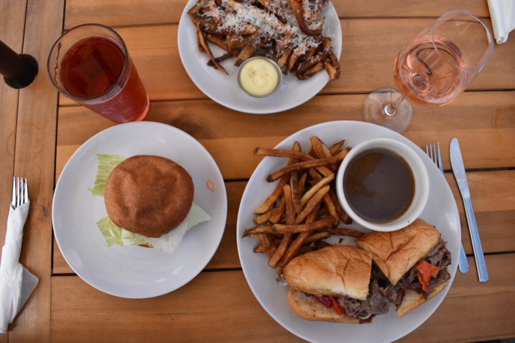 a table set with a burger, a french dip sandwich, fries, beer and wine