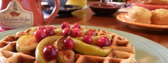 Hazelnut waffle topped with apples and cranberries, and a mug on a table