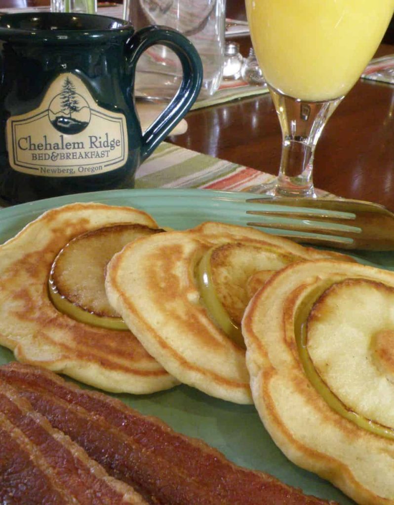 apple pancakes with bacon on a plate with a coffee mug and glass of orange juice