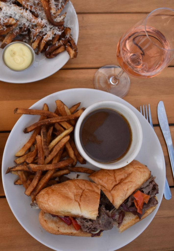Plates of french dip with a side of fried and a glass of rose wine