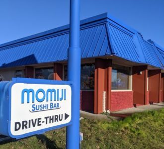 A sign saying Momiji Sushi Bar Drive-through and a building