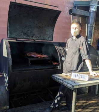 a man in front of a smoker with meat inside