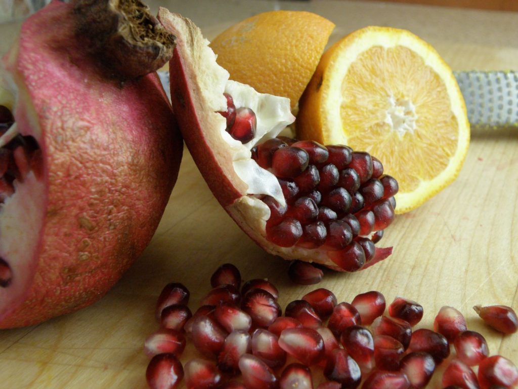 A pomegranate that has been split open and an orange cut in half on a cutting board