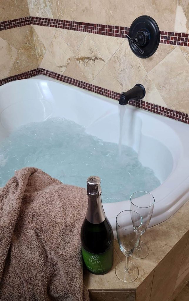 a 2 person jetted tub with a bottle of sparkling wine and glasses on the rim