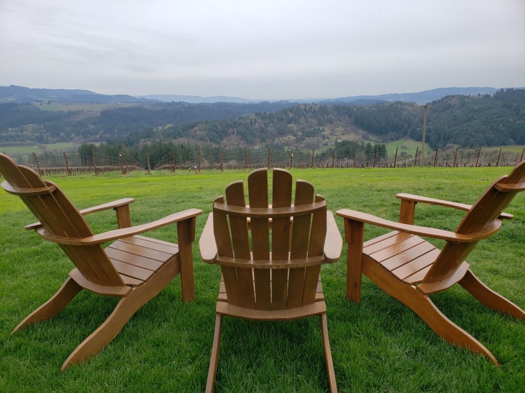 Three wooden Adirondack chairs on green grass with sprawling views of Willamette Valley wine country in Yamhill, Oregon