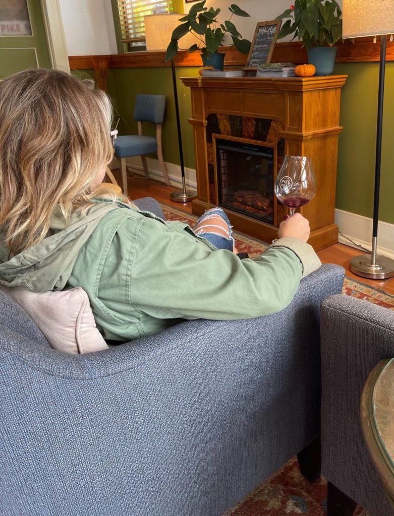 The inside of a wine tasting room in Carlton, Oregon. A woman in a chair with a glass of wine, facing a fireplace