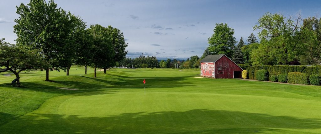 The greens of a Willamette Valley golf course with a small rustic red barn towards the background