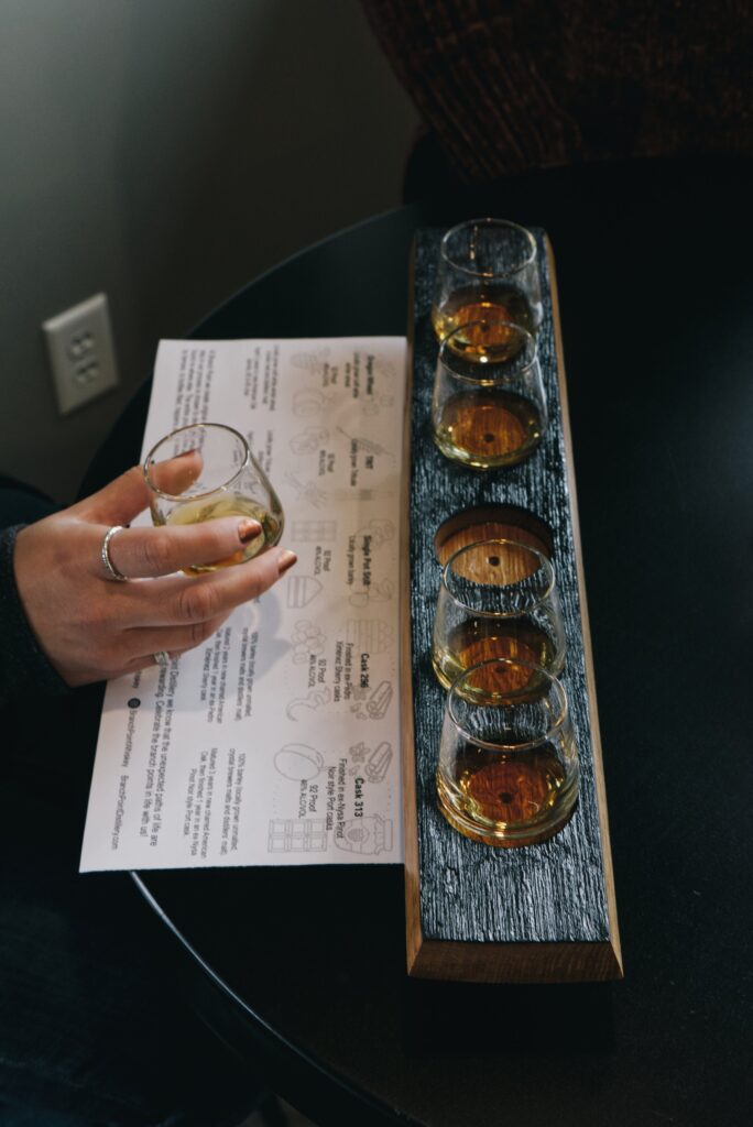 a wooden tray holding 5 small glasses of whiskey tastings, with a piece of paper describing each of the whiskeys at Branch Point Distillery, a willamette valley distillery