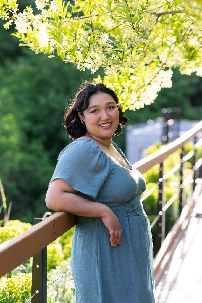 A woman leaning on a deck railing with tree foliage in the background