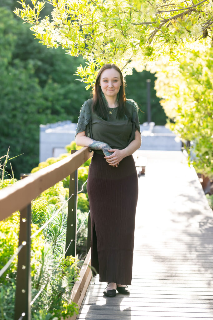 A woman leaning on a deck railing with tree foliage in the background