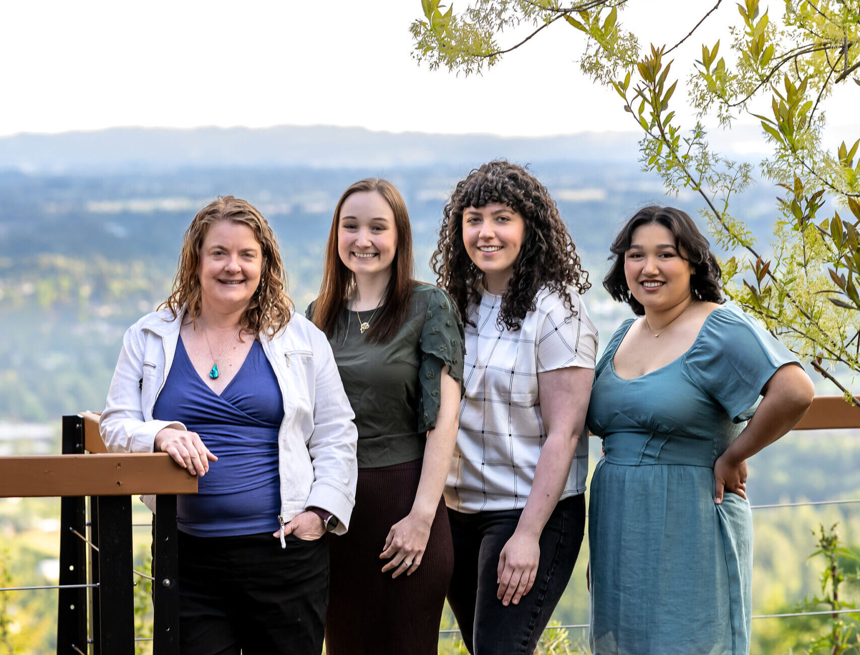 four women standing in front of a deck railing with the Willamette Valley in the distant background