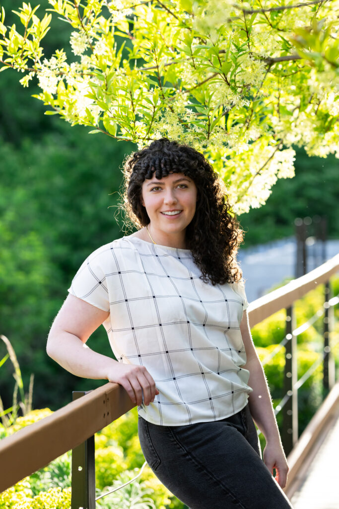A woman leaning on a deck railing with tree foliage in the background