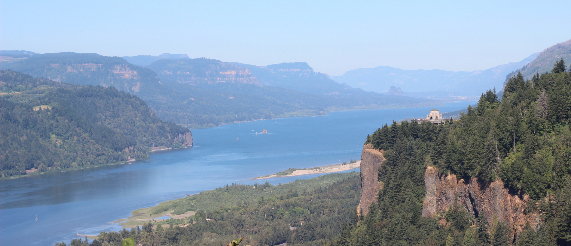 The Columbia River Gorge seen from Women's Forum State Scenic Overlook, with the river and the Vista House, an octagonal building, on a cliff to the right of the river