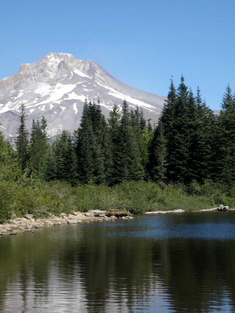 Mirror Lake in Mt Hood National Forest, with the lake in the foreground and mountain high above. The trees are reflected in the water of the lake
