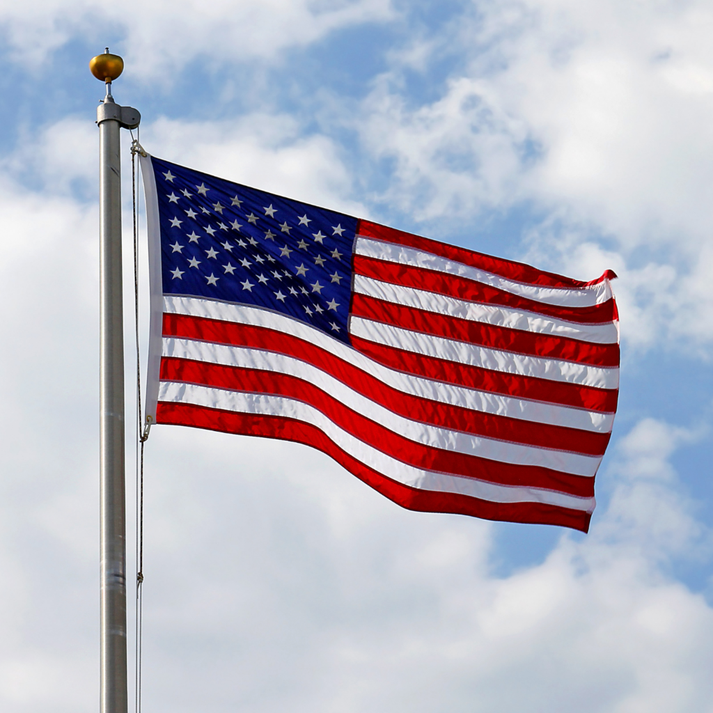 American flag waving in the wind. Set against a cloudy blue sky.