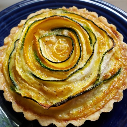 a small tart made with green and yellow zucchini in a spiral